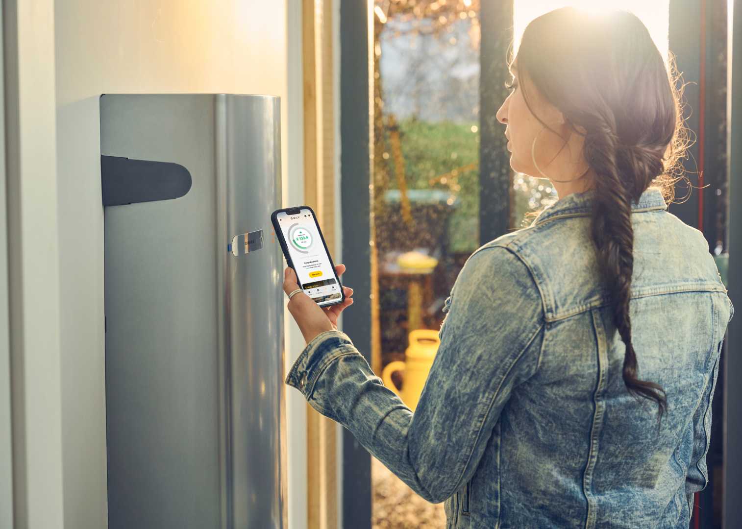Soly en Enphase bundelen krachten vrouw met telefoon bij thuisbatterij