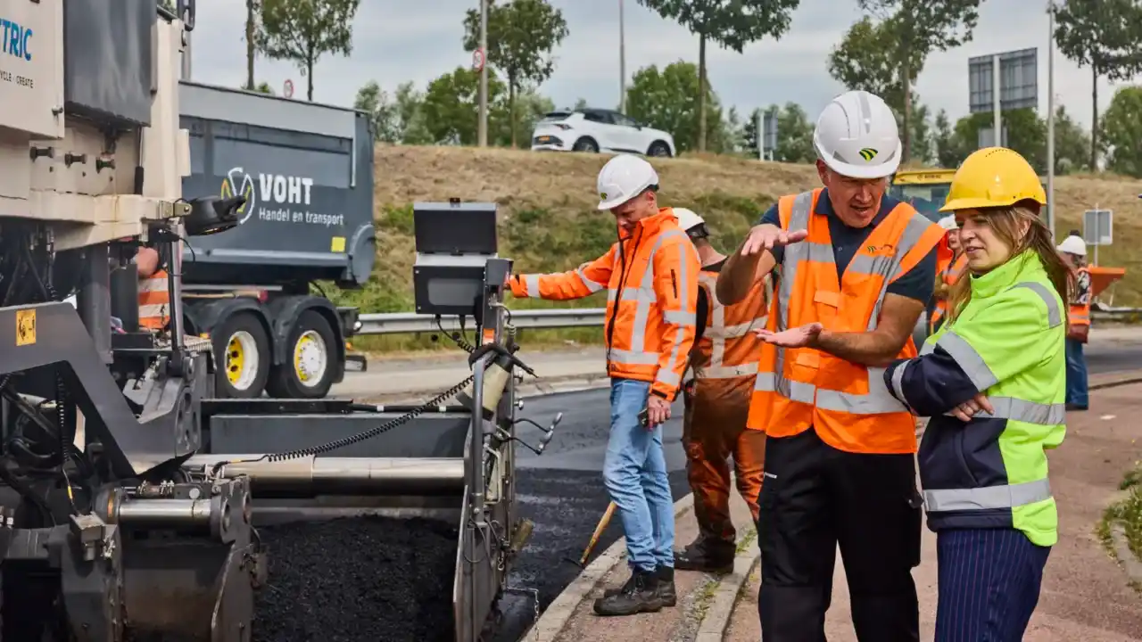 Man geeft uitleg aan vrouw bij asfalt werkzaamheden