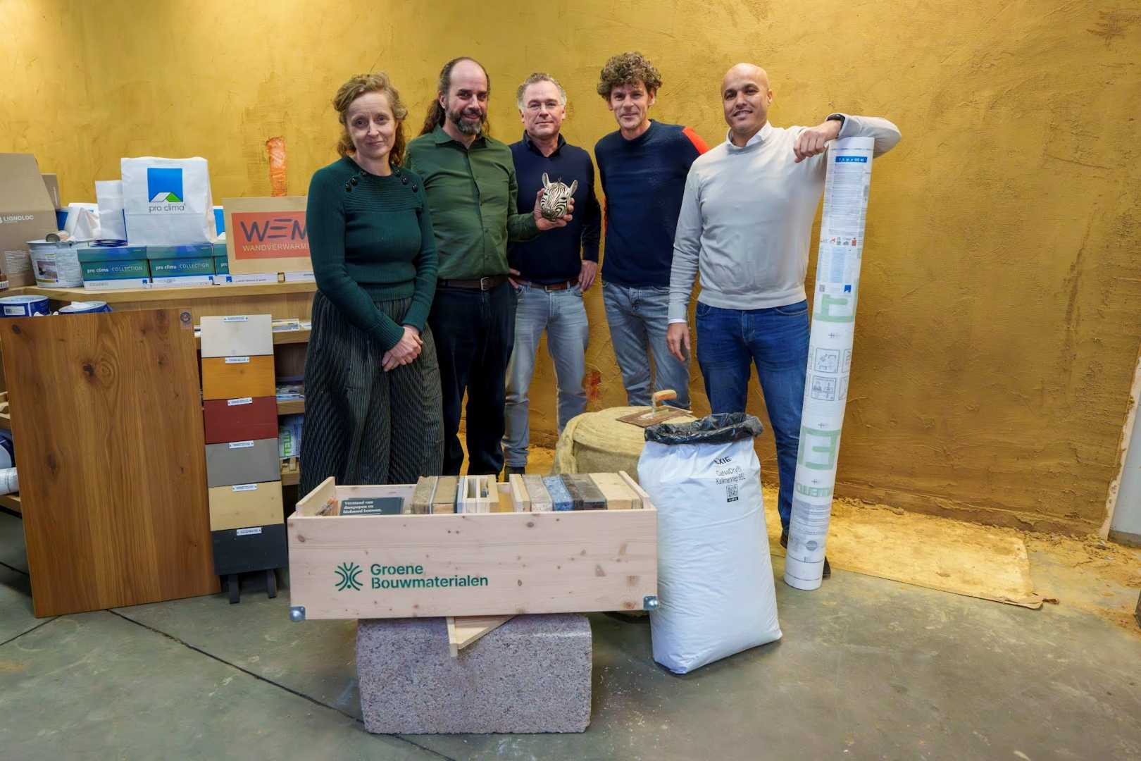 4 mannen en vrouw poseren bij bouwmaterialen